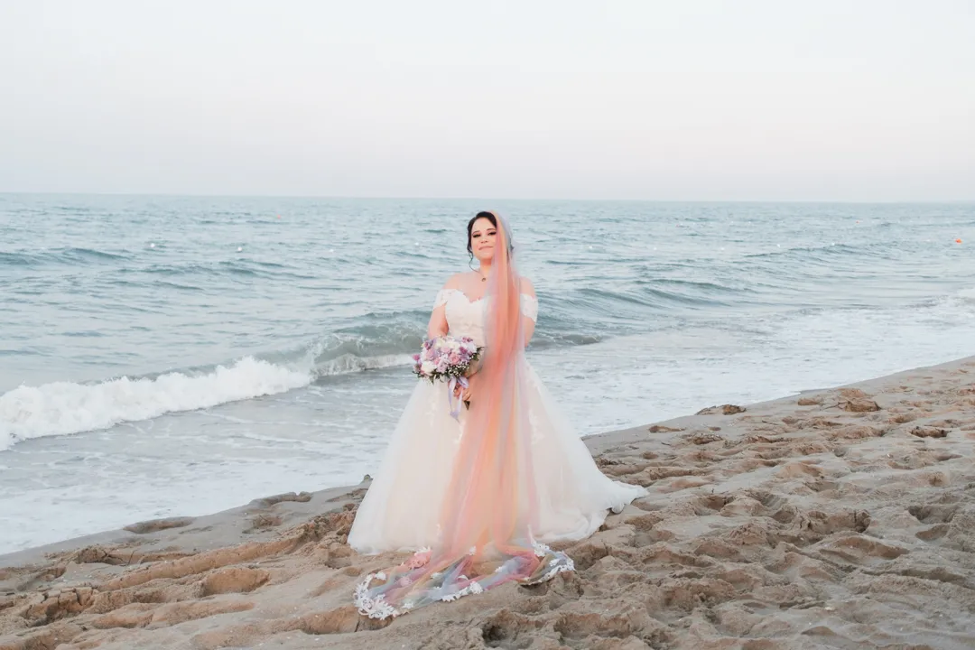 Noiva à beira-mar com vestido e véu em tons suaves